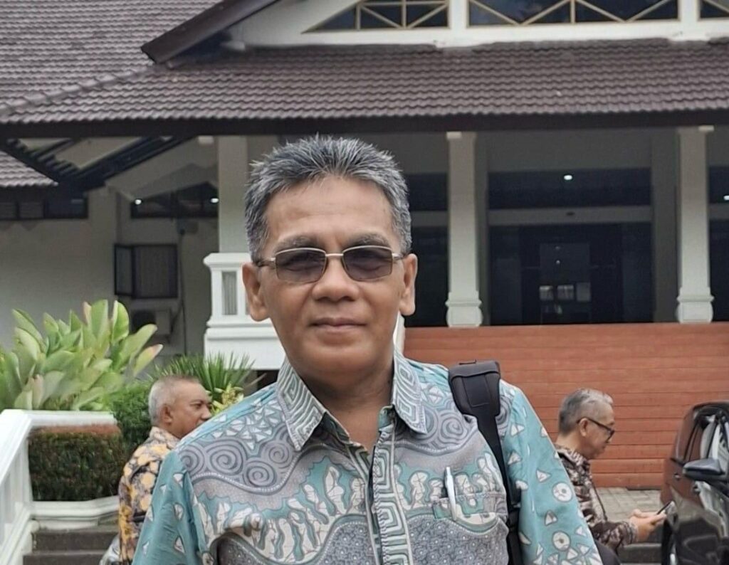 Man wearing sunglasses and a patterned teal shirt standing outside a building with a backpack strap visible on his shoulder